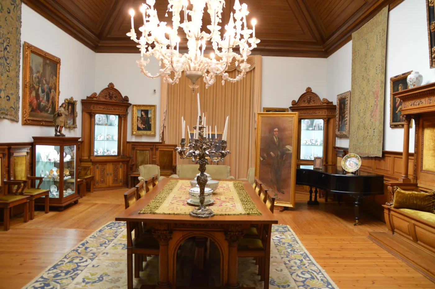 Salão Nobre da Casa dos Patudos, com lustre de cristal, grande mesa central, vitrines de porcelana, tapeçarias e o retrato de José Relvas